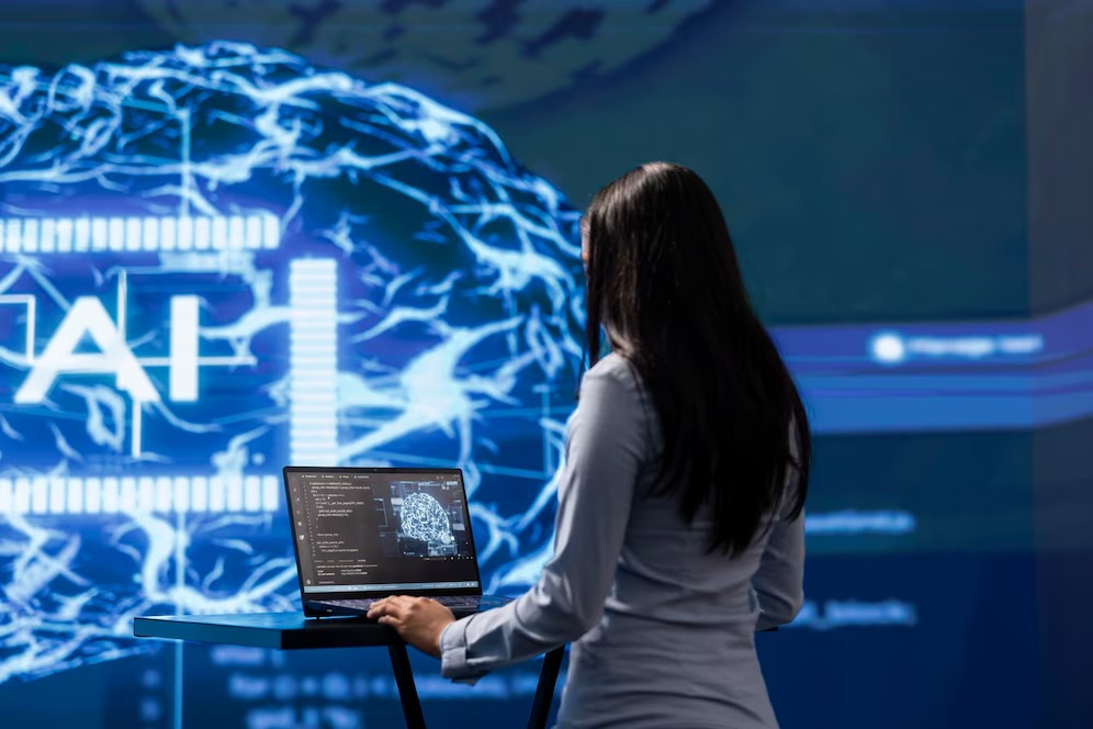  A woman with long hair stands in front of a digital brain visual, working on a laptop displaying AI-related data and code.