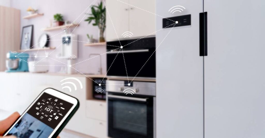 A smartphone displays IoT controls while connected to a modern kitchen with smart appliances, illustrating smart home technology.