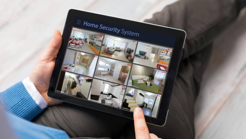 A person using a tablet to monitor home security, displaying multiple camera feeds of various rooms in a house.