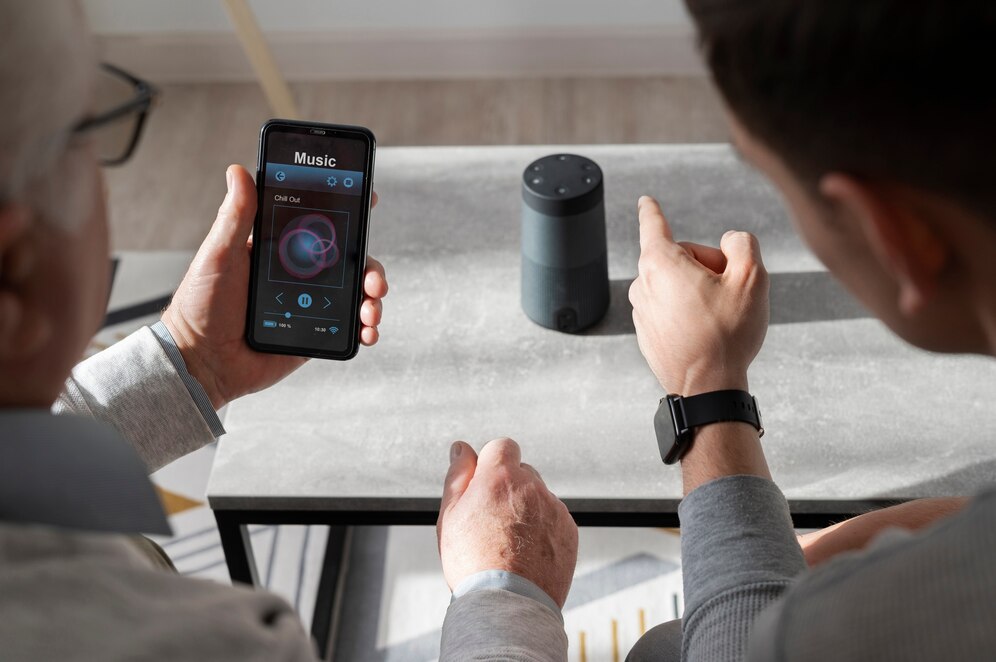 A smartphone displaying a music app, while the other gestures towards a smart speaker on the table.