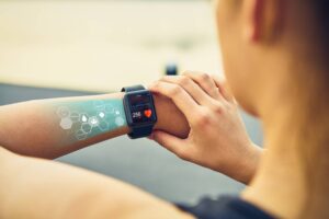 A woman checking her fitness smartwatch displaying heart rate and activity metrics, with digital health icons projected on her arm.