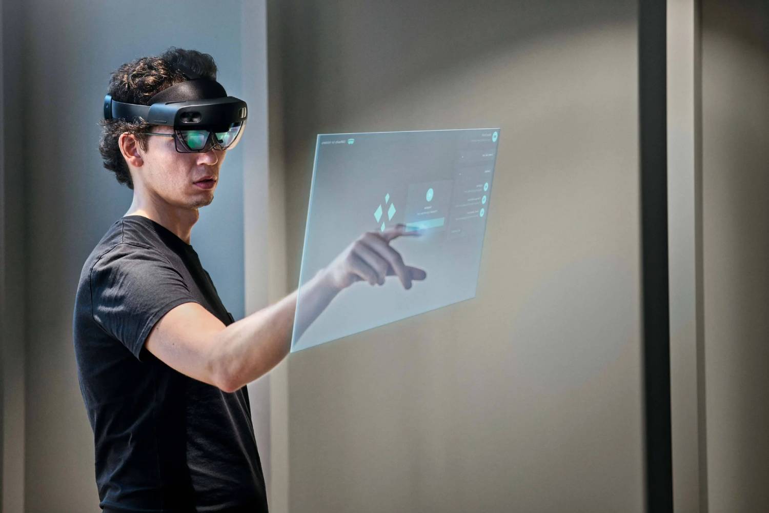  A person wearing augmented reality glasses interacts with a transparent holographic interface displayed on a wall.