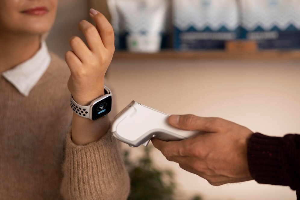  A woman with light skin is using a smartwatch to make a payment with a card reader held by a person in a dark sweater.