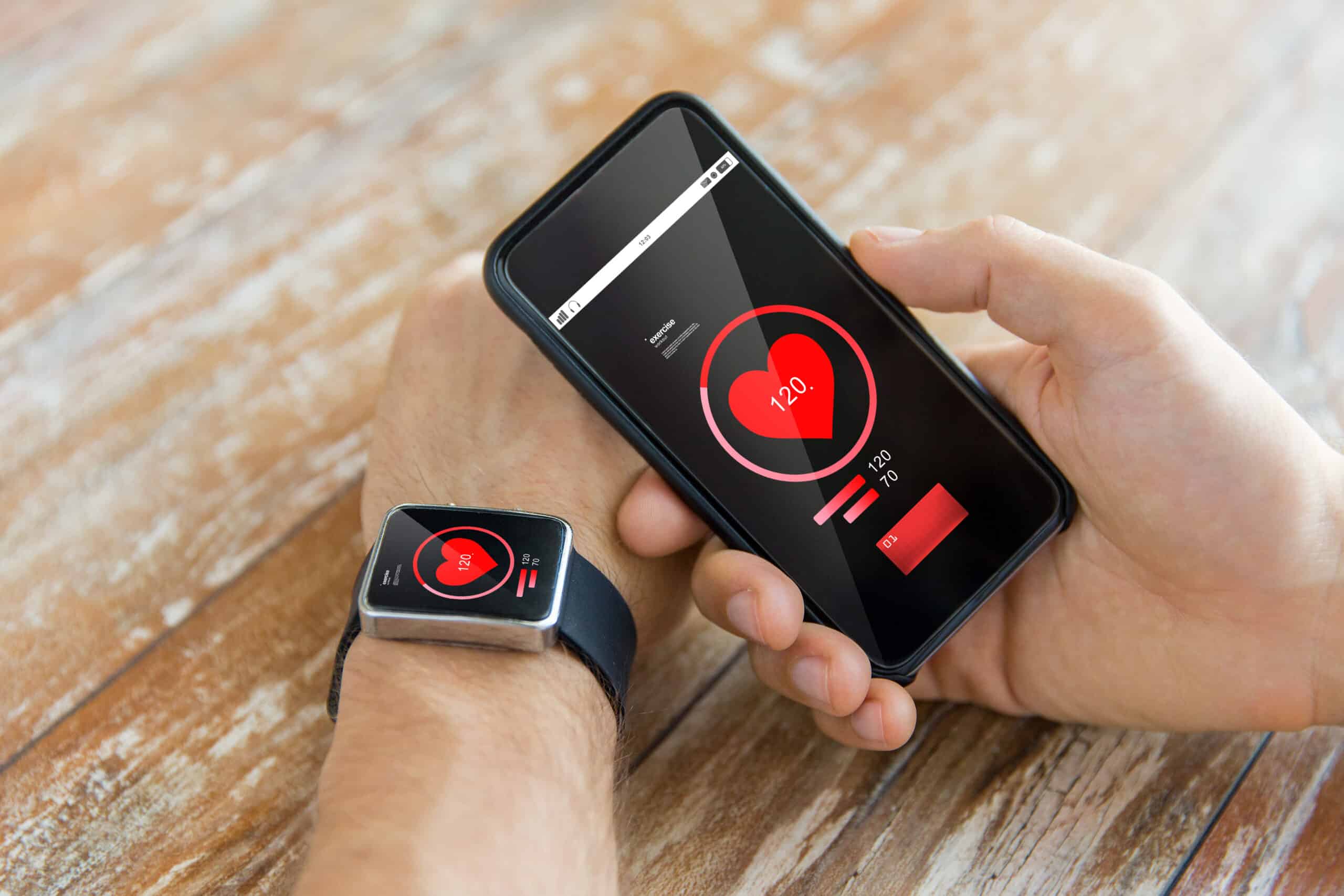  A person checks their heart rate on a smartphone and smartwatch, displaying a reading of 120 BPM against a wooden table.