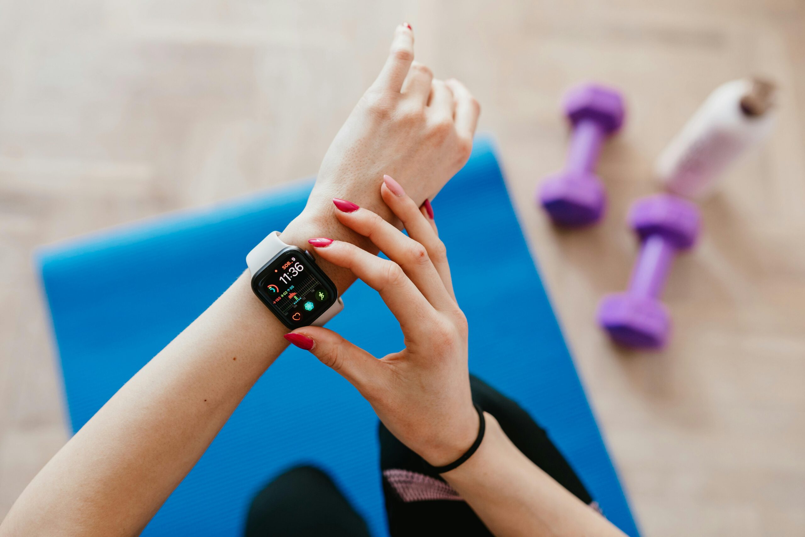 A close-up of a hand checking a smartwatch displaying fitness stats, with workout equipment in the background on a blue mat.