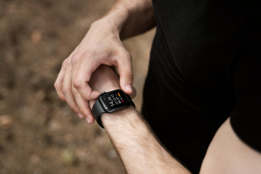 A close-up of a person wearing a smartwatch on their wrist, checking fitness stats in an outdoor setting.