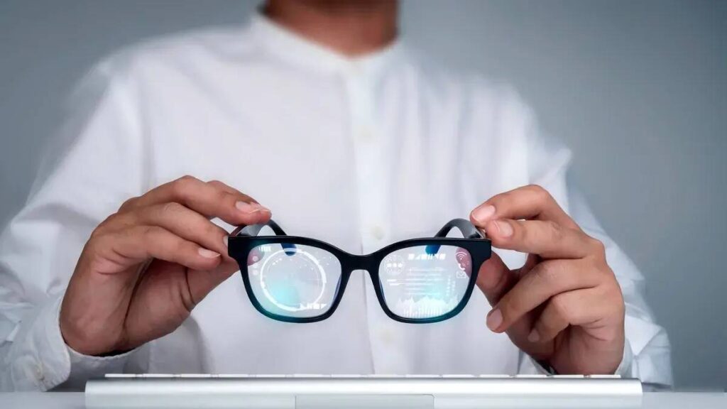 A person in a white shirt holds smart glasses displaying digital graphics, with a keyboard visible in the foreground.