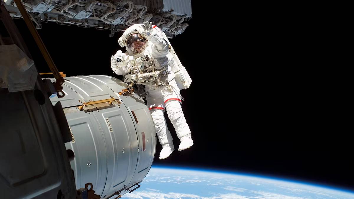 An astronaut performs a spacewalk outside the International Space Station, floating against a backdrop of Earth and deep space.